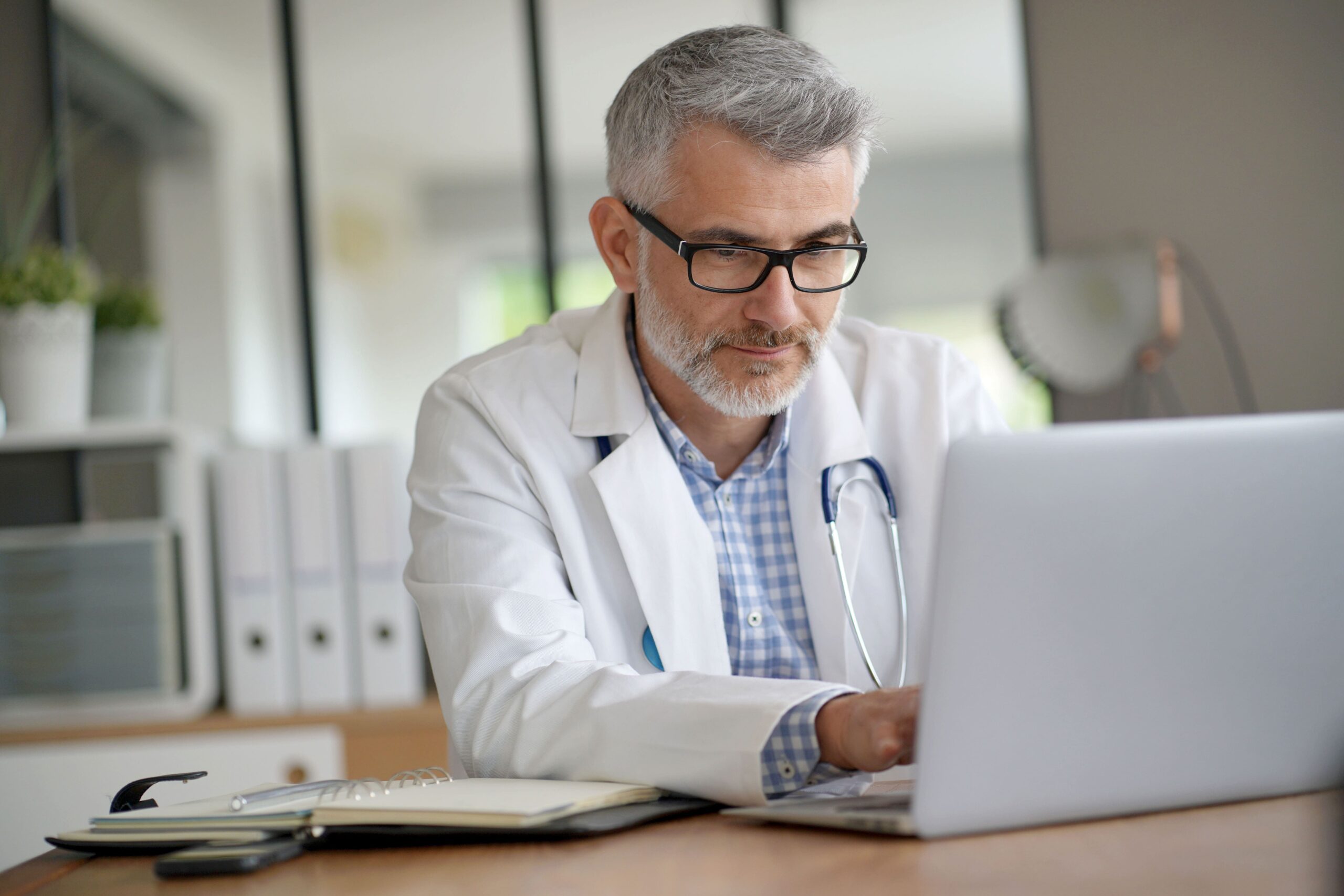 A medical professional in a white coat on his laptop in a rural healthcare practice uses big bandwith from Kinetic Business
